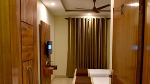 A hotel room with a bed, a TV on a stand, wooden wardrobes, a ceiling fan, and a curtain. - Hotel Triveni Residency Near SMS Stadium (Jaipur)