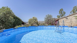 Una piscina azul cristalina con borde de azulejos, rodeada de follaje y un muro de piedra.