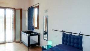 Un dormitorio con cama, un escritorio pequeño, una silla, una ventana con cortinas y un espejo en la pared.