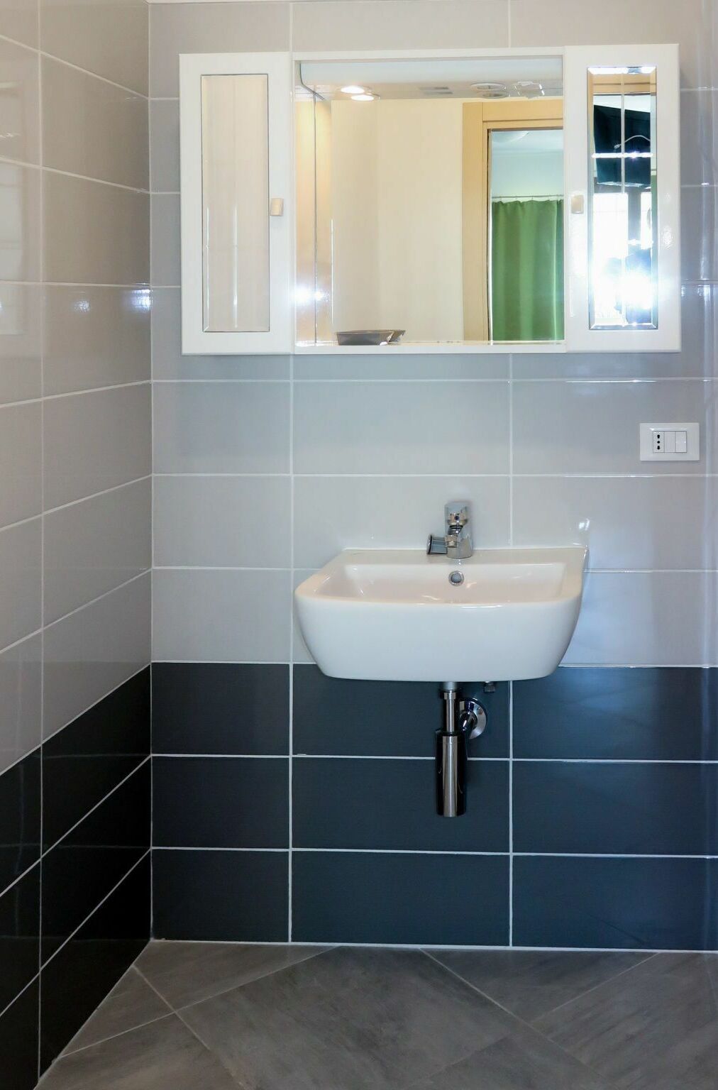A bathroom with a white sink, dark tiled walls, and a mirror above the sink.