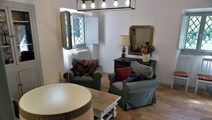 A cozy living room with a sofa, a table, and a lamp. There is a window with a view of greenery outside. - The Apartment · Casa del Fattore, Villa Luzi (Marche)