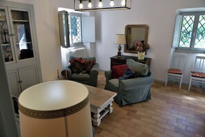 A cozy living room with a sofa, a table, and a lamp. There is a window with a view of greenery outside. - The Apartment · Casa del Fattore, Villa Luzi (Marche)