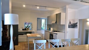 A modern kitchen with white cabinetry, a dining area with a wooden table and white chairs, and a window providing natural light. - The Apartment · Casa del Fattore, Villa Luzi (Marche)