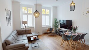 A modern living room with a leather sofa, a coffee table, a TV, and a dining area with a glass table and chairs. - MyHappyplace in the middle of Berlin (Berlin)