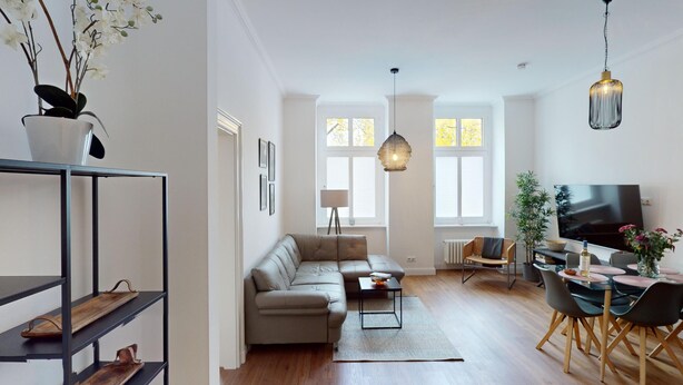A modern living room with a sofa, coffee table, and dining area. There is a TV, a plant, and a shelf with shoes. - MyHappyplace in the middle of Berlin (Berlin)