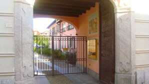 Una entrada portonada con un portón metálico, un arco de piedra y un edificio de fachada rosa con un balcón.