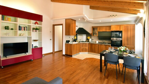 Una cocina moderna con armarios de madera, un comedor con una mesa para dos personas, y una sala de estar con una televisión de pantalla plana y un mueble de entretenimiento rojo.