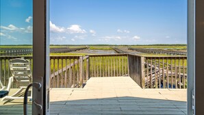 Eine Holzterrasse, die zu einer Brücke über ein Gewässer führt, mit sichtbaren Stühlen und einem Geländer.