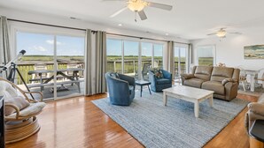 Ein geräumiges Wohnzimmer mit großem Fenster, Deckenventilator und Blick auf einen Steg und Wasser.