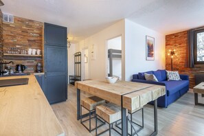 A modern kitchen with a wooden table and stools, a blue sofa, and a wooden accent wall.