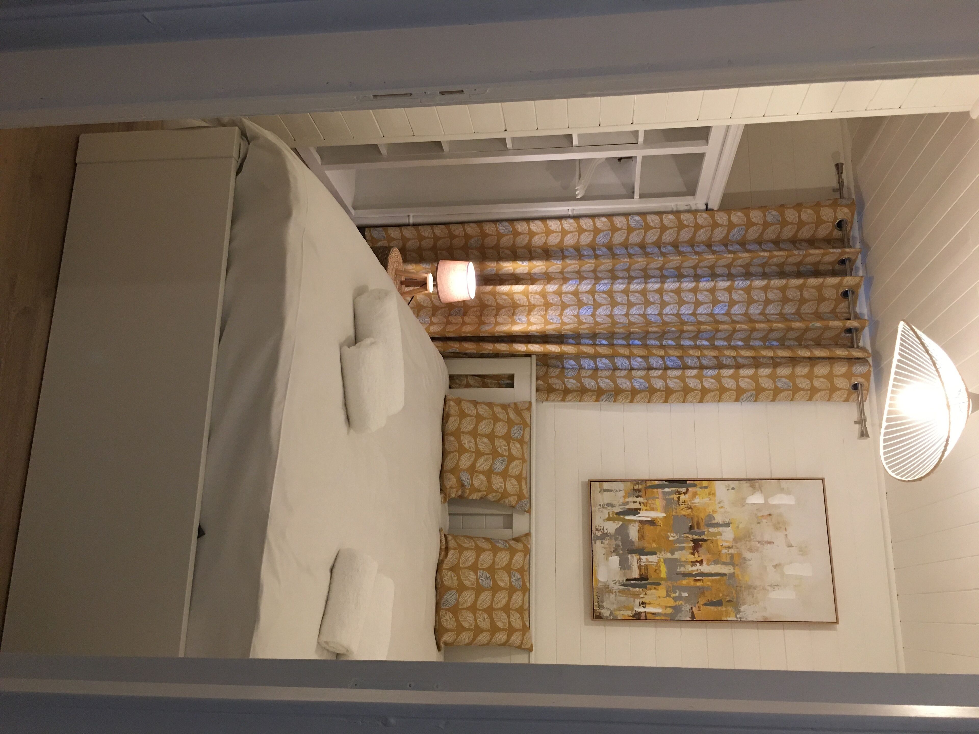 Una habitación con una cama, un papel tapiz estampado, un cuadro y un ventilador de techo.
