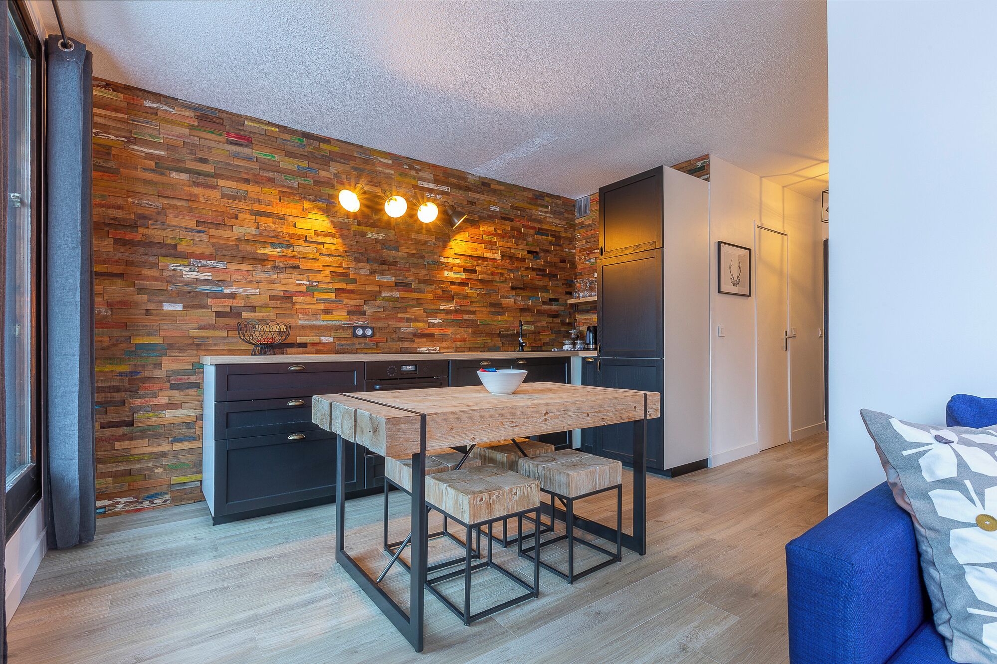 A modern kitchen with a wooden plank backsplash, a central island, and black cabinetry.