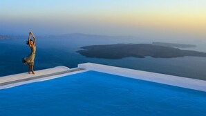Une personne effectuant une posture de yoga sur le bord d’une piscine à débordement située sur un toit, avec une vue sur la côte.