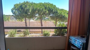 Ein Balkon mit Blick auf Bäume und Gebäude, ein Tisch mit einem gemusterten Tischläufer und eine Hängematte.