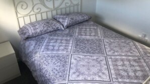 A small, single-bed room with a metal headboard, a patterned bedspread, and a nightstand. - Inviting 2-bed Apartment in Hemsby (Great Yarmouth)