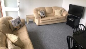 A living room with a beige sofa, a small table, a television, and a chair. - Inviting 2-bed Apartment in Hemsby (Great Yarmouth)