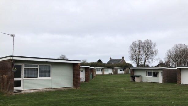 A row of mobile homes with a grassy yard and a distant house. - Inviting 2-bed Apartment in Hemsby (Great Yarmouth)