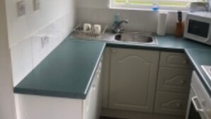 A compact kitchen with white cabinets, a microwave, and a sink. - Inviting 2-bed Apartment in Hemsby (Great Yarmouth)