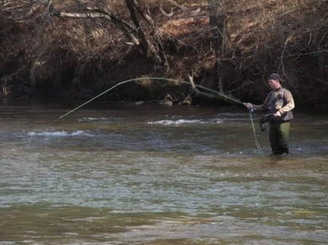 Una persona de pie en un río, sosteniendo una caña de pescar.