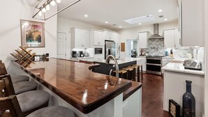 Een moderne keuken met witte kasten, een houten keukeneiland met barstoelen, een roestvrijstalen spoelbak en een hangende lamp.