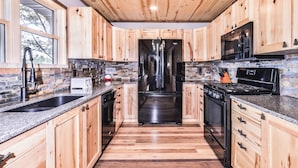 Cocina moderna con armarios de madera, refrigerador de acero inoxidable, microondas, estufa y encimeras de granito.