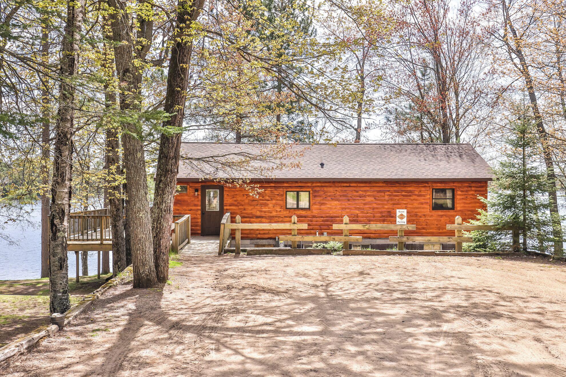 A rustic cabin with a wooden deck, a dock, and a sign indicating guest parking.