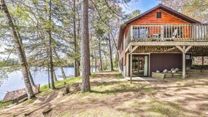 Una cabaña con terraza con vista a un lago, rodeada de árboles.