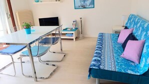 Een moderne kamer met een blauwe gestreepte bank, een eettafel met stoelen, een kleine televisie en een klok aan de muur.