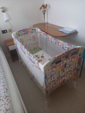 Ein Babybett mit farbig gestepptem Muster, ein kleiner Tisch mit einer Vase und eine Lampe.