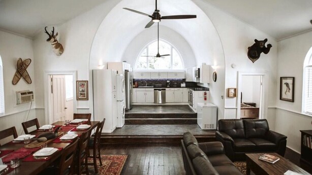 A spacious living area with a dining table set for four, a leather sofa, and a kitchen in the background. - THE OLD CHURCH INN is a luxurious Property near Salmon River (Altmar)