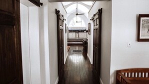 A narrow hallway with wooden floors and white walls, leading to a kitchen area with a skylight and a ceiling fan. - THE OLD CHURCH INN is a luxurious Property near Salmon River (Altmar)