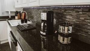 A modern kitchen with white cabinets, a black countertop, a coffee machine, and a coffee grinder. - THE OLD CHURCH INN is a luxurious Property near Salmon River (Altmar)