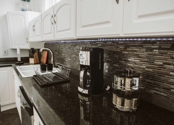 A modern kitchen with white cabinets, a black countertop, a coffee machine, and a coffee grinder.