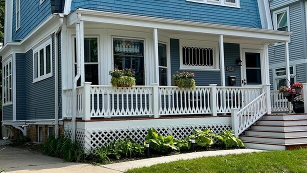 A two-story house with a blue exterior, white trim, and a front porch with a white picket fence.