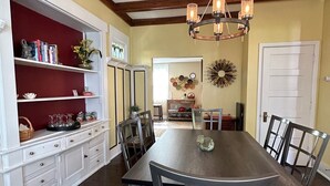 A dining room with a large wooden table, dark chairs, a chandelier, and a red wall with shelves.