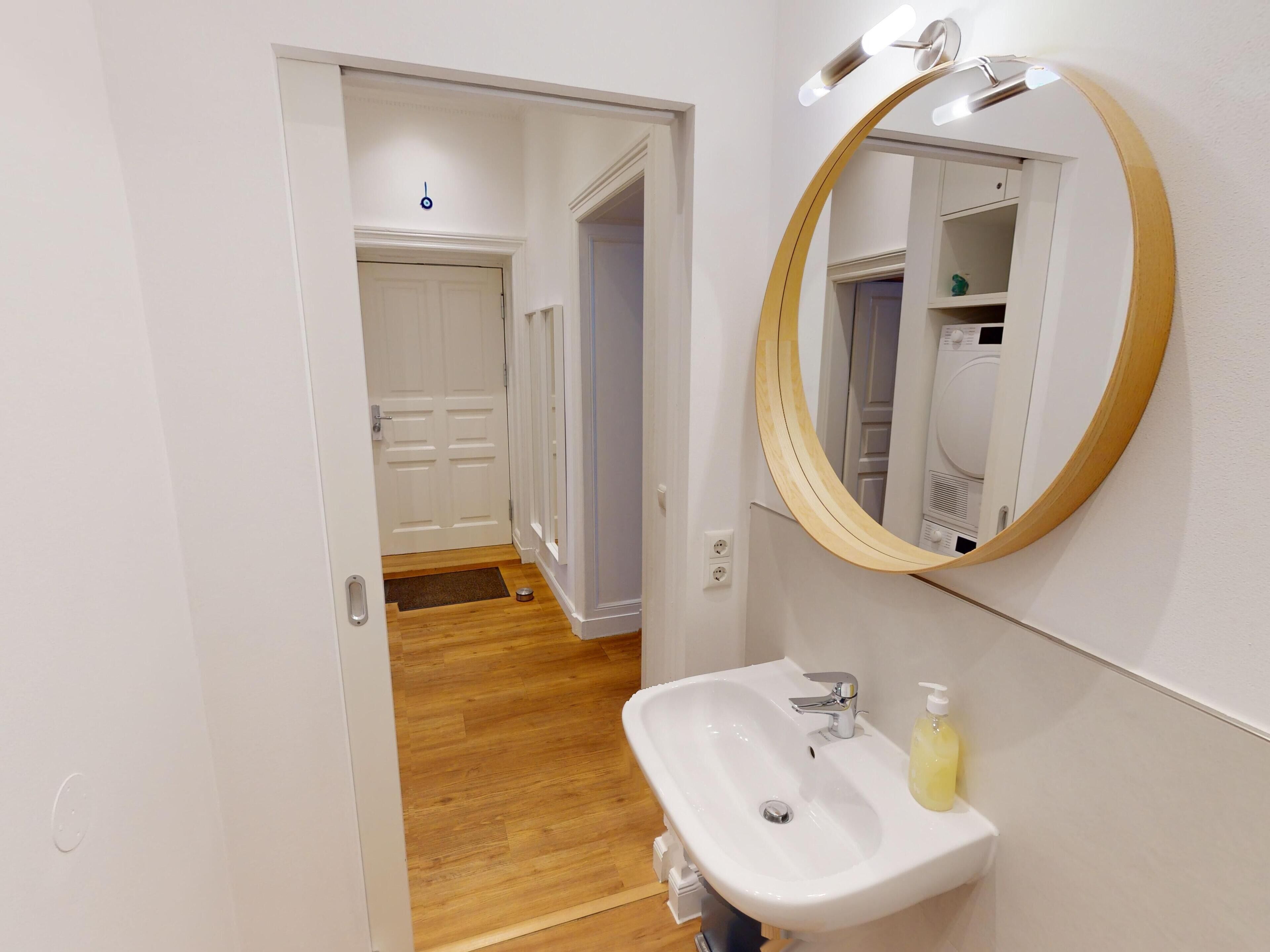 Un bagno con un lavandino bianco, uno specchio con cornice in legno e una porta che dà su un'altra stanza.