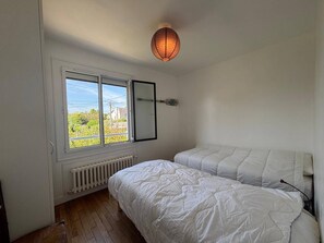 A bedroom with a bed, a window, a radiator, and a hanging light fixture.