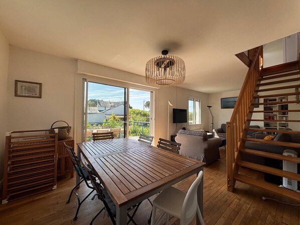 A spacious living area with a wooden dining table, a sofa, and a staircase.
