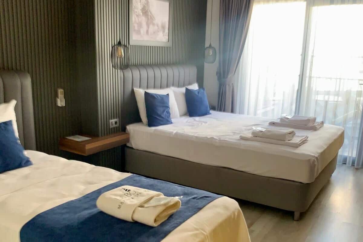 A hotel room with two beds, a large window with curtains, and a wall-mounted artwork.