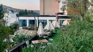 Un espace extérieur aménagé avec des tables et des parasols, entouré de verdure et offrant une vue sur un paysage vallonné.