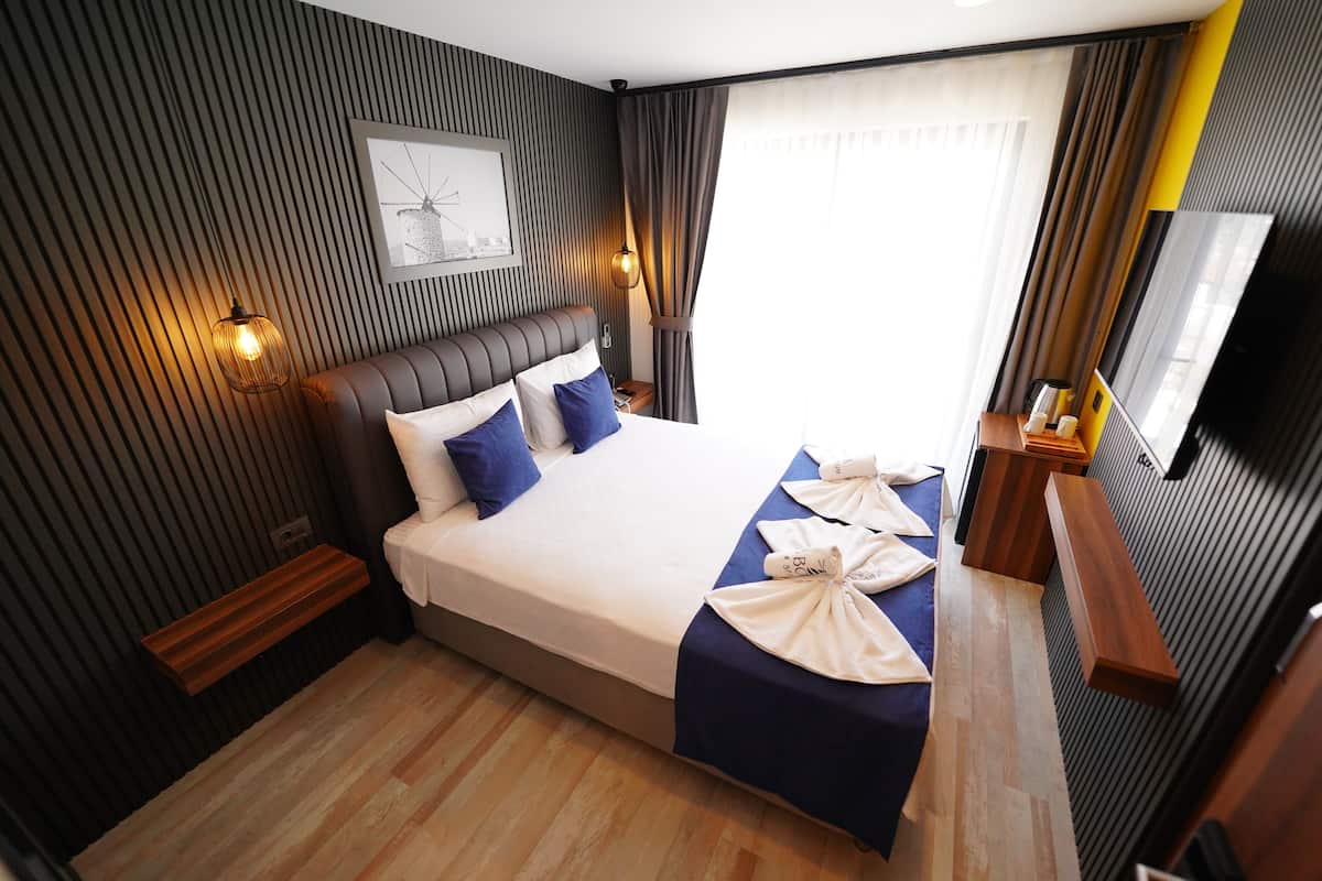 A modern hotel room with a large bed, a wooden nightstand, a bedside table, a flat-screen TV, and a wall-mounted artwork.