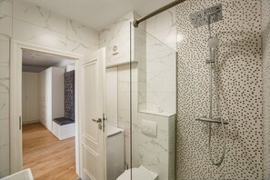 A modern bathroom with a glass-enclosed shower, marble walls, and a wooden floor. - Fantastic Apartment at Prima Residence (Oradea)