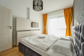 A modern bedroom with a bed, a wardrobe, and a window with curtains. - Fantastic Apartment at Prima Residence (Oradea)