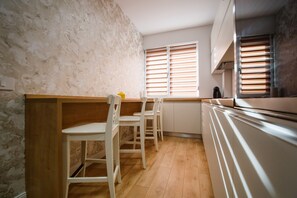 A kitchen with wooden cabinets, a white countertop, and a window with blinds. - Fantastic Apartment at Prima Residence (Oradea)
