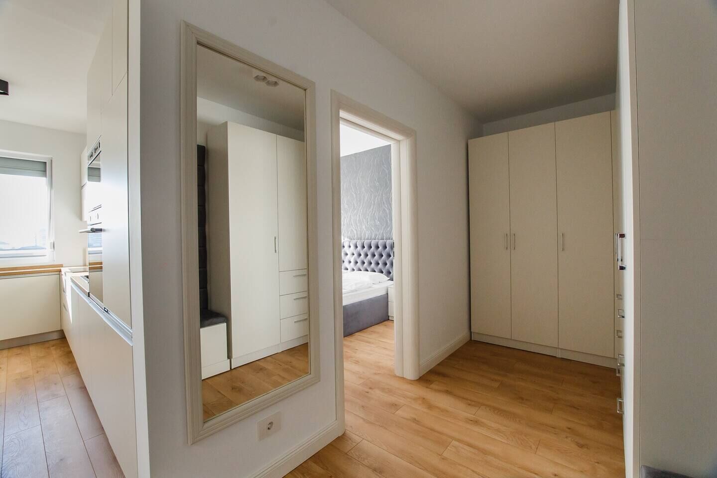 A modern bedroom with a large mirror, a wardrobe, and a view of a balcony.