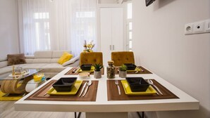 Un salon moderne avec un canapé, une table à manger pour deux personnes et un téléviseur fixé au mur.