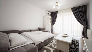 A modern bedroom with a grey sofa bed, a white desk, and a patterned rug. - Bright & Elegant Central Apartment (Oradea)