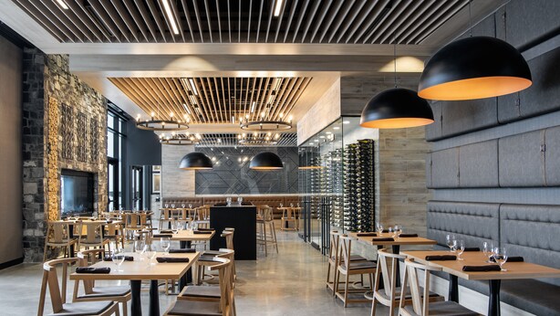A modern restaurant with wooden tables and chairs, a stone wall, and a long counter with wine glasses. - Dakota Dunes Resort (Whitecap)
