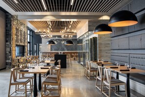 A modern restaurant with wooden tables and chairs, a stone wall, and a long counter with wine glasses. - Dakota Dunes Resort (Whitecap)
