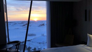 A hotel room with a large window offering a view of a snowy landscape and a sunset. - Dakota Dunes Resort (Whitecap)